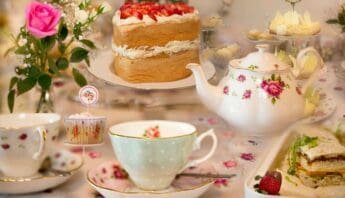 Scones with strawberries, tea set, and desserts on a floral tablecloth for an elegant afternoon tea gathering.
