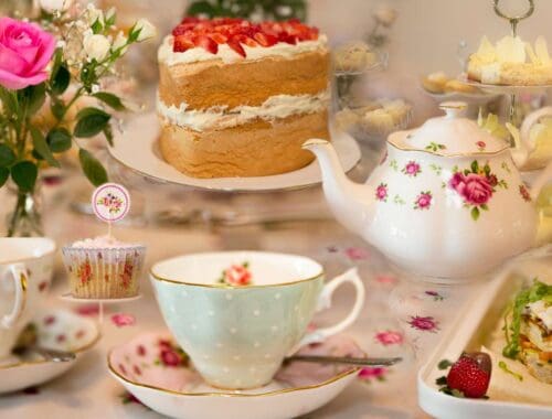 Scones with strawberries, tea set, and desserts on a floral tablecloth for an elegant afternoon tea gathering.