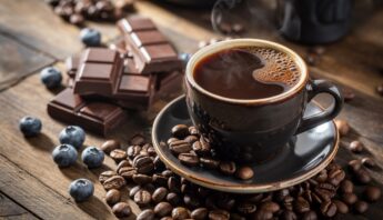 Rich, dark coffee with scattered coffee beans and chocolate pieces on a rustic wooden surface.