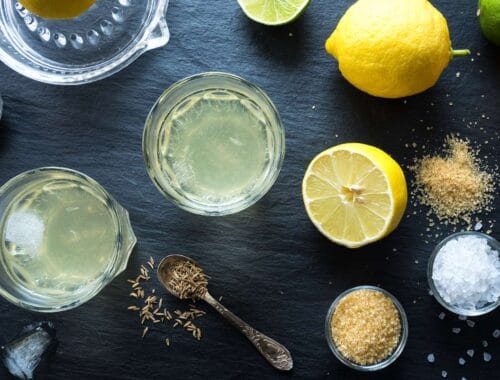 Lemon water with fresh lemons, salt, and spices on a dark surface, highlighting healthy hydration and natural detox options.