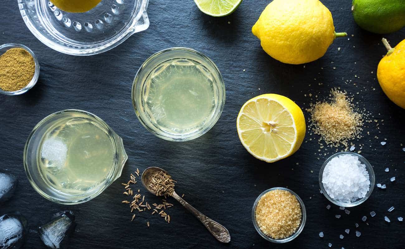 Lemon water with fresh lemons, salt, and spices on a dark surface, highlighting healthy hydration and natural detox options.