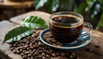 Rich black coffee in a glass cup with steam on a rustic wooden table surrounded by coffee beans and green leaves.