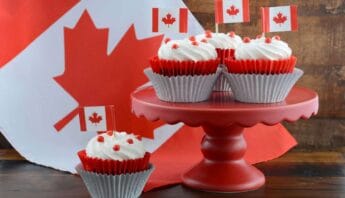 Cupcakes with Canadian flags on a pink cake stand and a maple leaf background, celebrating Canada Day with themed desserts, festive atmosphere, and patriotic decorations.