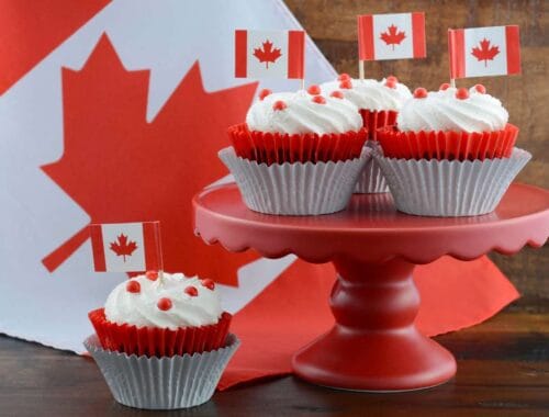 Cupcakes with Canadian flags on a pink cake stand and a maple leaf background, celebrating Canada Day with themed desserts, festive atmosphere, and patriotic decorations.