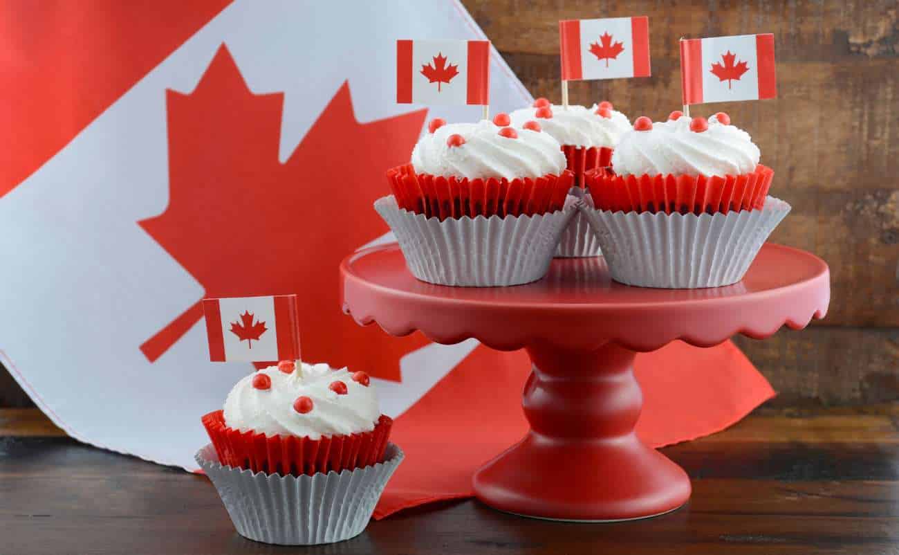 Cupcakes with Canadian flags on a pink cake stand and a maple leaf background, celebrating Canada Day with themed desserts, festive atmosphere, and patriotic decorations.