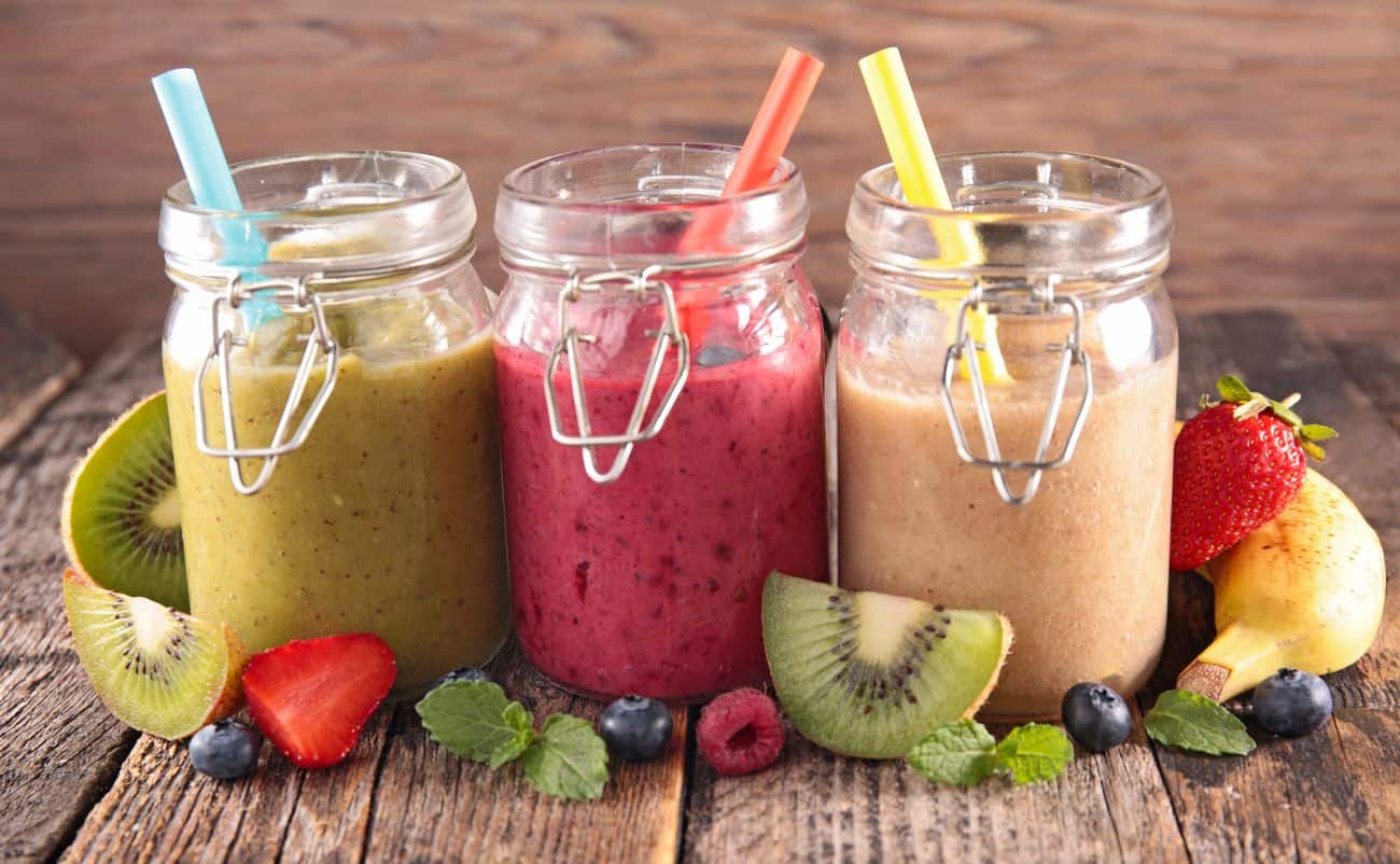Refreshing fruit smoothies in glass jars with colorful straws on a rustic wooden surface, surrounded by fresh fruits like strawberries, kiwi, blueberries, raspberries, and bananas. Healthy and delicious beverage options for a nutritious lifestyle.