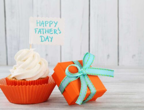 Delicious cupcake with white frosting and a "Happy Father's Day" note on top, placed next to an orange gift box with a green ribbon, celebrating Father's Day with sweet treats and thoughtful presents.