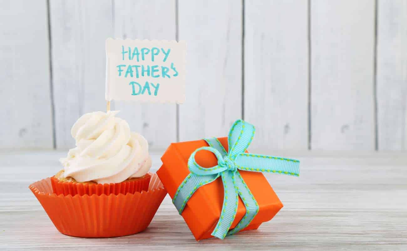 Delicious cupcake with white frosting and a "Happy Father's Day" note on top, placed next to an orange gift box with a green ribbon, celebrating Father's Day with sweet treats and thoughtful presents.