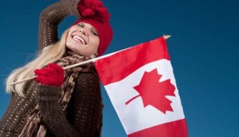 10 Delicious Easy Canada Day Recipe Ideas to Celebrate in Style! 15 Canada flag being held by a smiling woman wearing winter clothing on a blue sky background.