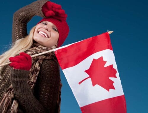 Canada flag being held by a smiling woman wearing winter clothing on a blue sky background.