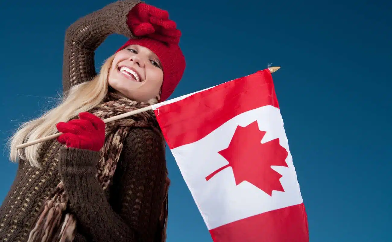 Canada flag being held by a smiling woman wearing winter clothing on a blue sky background.