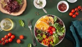 Fresh colorful vegetable salad with cherry tomatoes, cucumbers, carrots, mixed greens, and dressing on a green rustic background.
