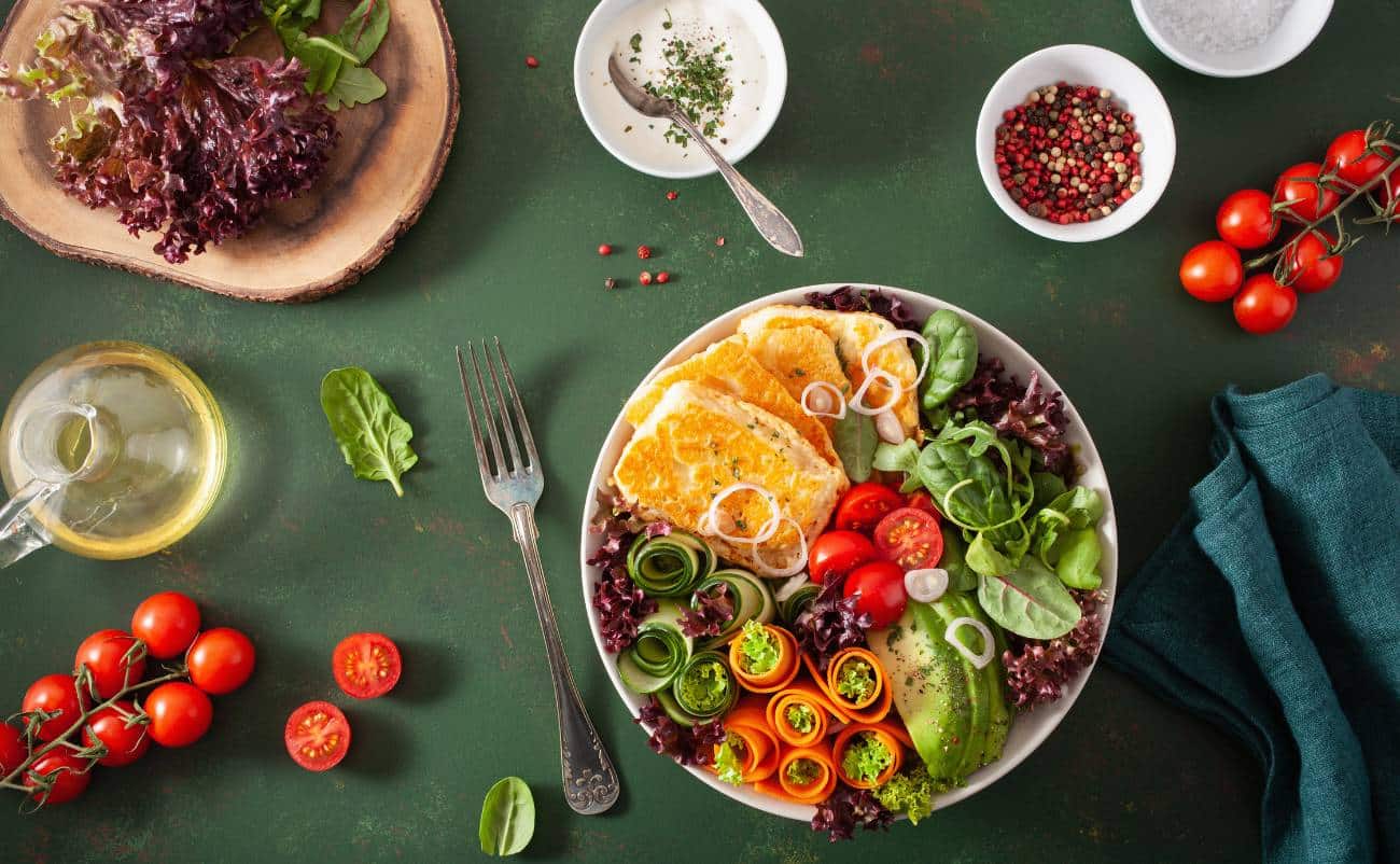 Fresh colorful vegetable salad with cherry tomatoes, cucumbers, carrots, mixed greens, and dressing on a green rustic background.