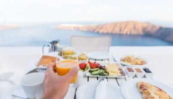 Fresh breakfast with juice, fruits, pizza, and coffee overlooking a scenic landscape, promoting healthy lifestyle and balanced diet.