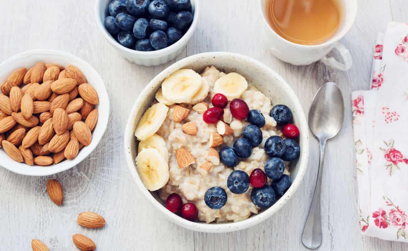 Almond oatmeal bowl with blueberries, bananas, and red currants on a white wooden table, healthy breakfast, nutritious food, fitness meal, Start to Fit website.