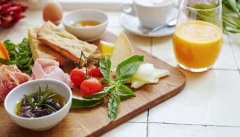 Fresh healthy breakfast with cherry tomatoes, olives, cheese, crostini, orange juice, tea, and eggs on a wooden board for balanced nutrition and wellness.