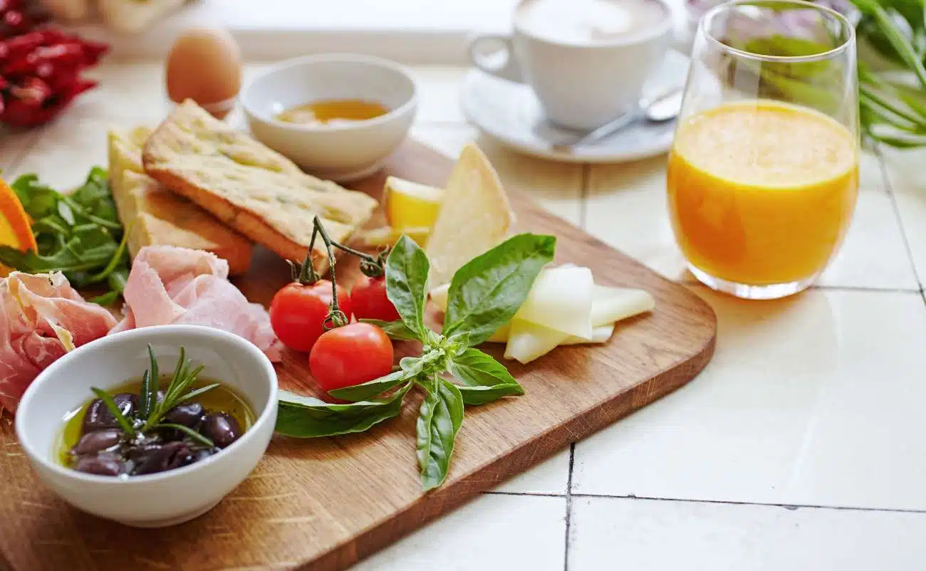 Fresh healthy breakfast with cherry tomatoes, olives, cheese, crostini, orange juice, tea, and eggs on a wooden board for balanced nutrition and wellness.
