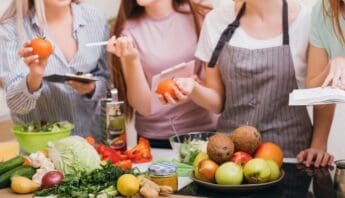 Fresh vegetables and fruits on a kitchen counter with people learning about healthy cooking and nutrition.