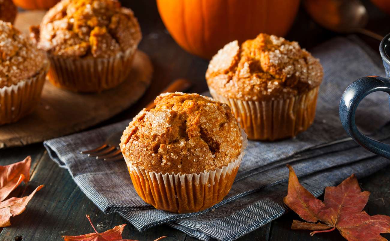 Pumpkin muffins with cinnamon sugar topping on a rustic wooden table surrounded by autumn leaves.