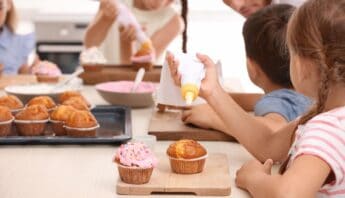 Freshly baked cupcakes being decorated and enjoyed by children at a baking party in a home kitchen setting.