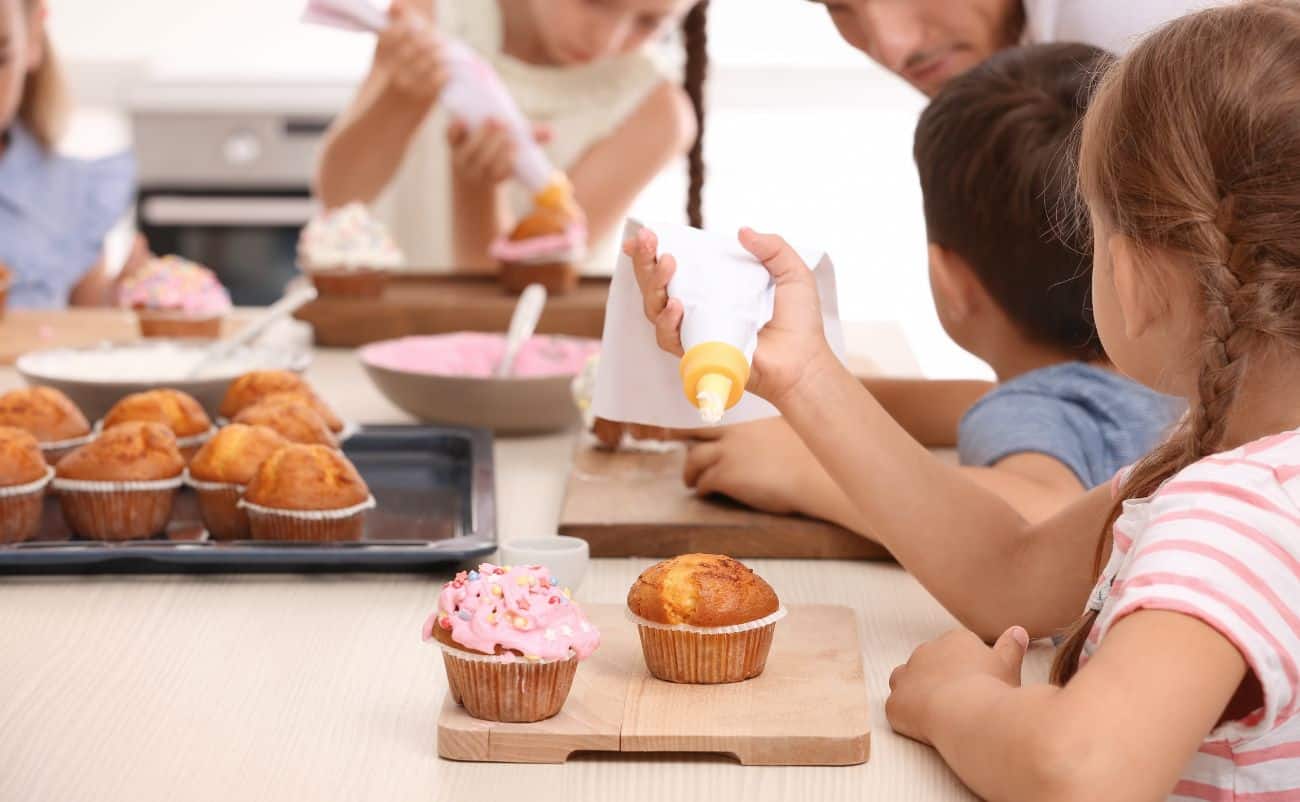 Freshly baked cupcakes being decorated and enjoyed by children at a baking party in a home kitchen setting.
