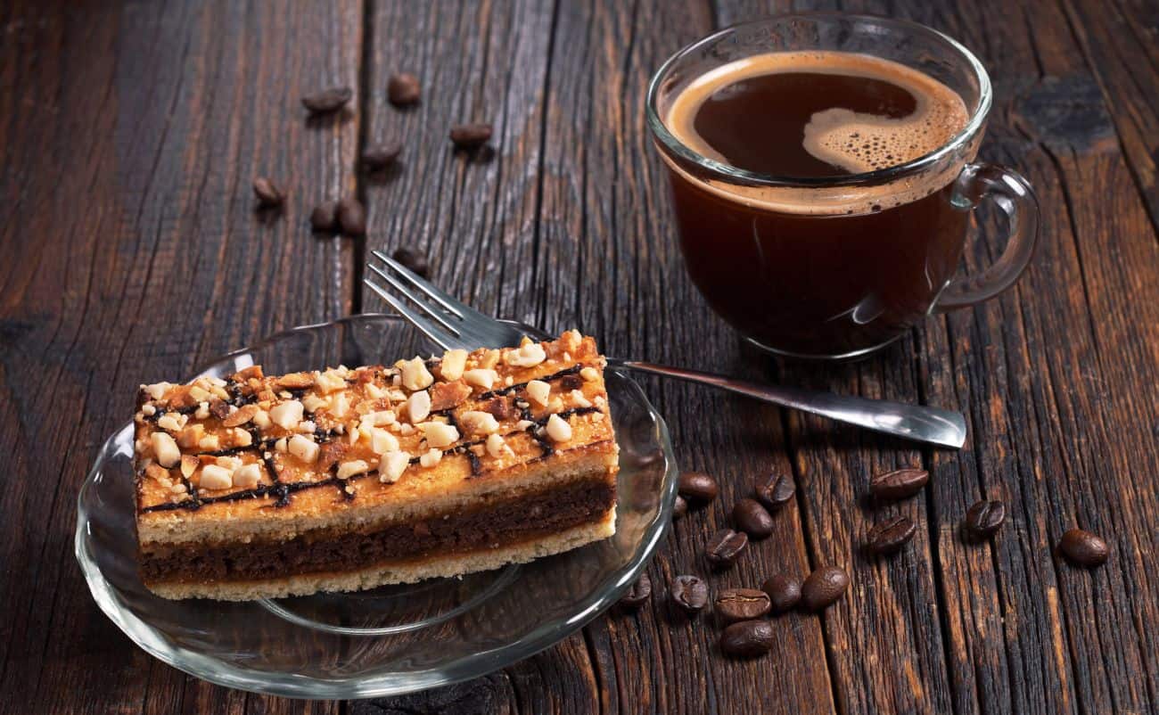 Rich coffee in a glass cup next to a layered chocolate cake slice on a dark wooden table.