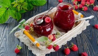Fresh homemade raspberry jam in glass jars with raspberries and green leaves on a rustic wooden table for healthy eating and natural preserves.
