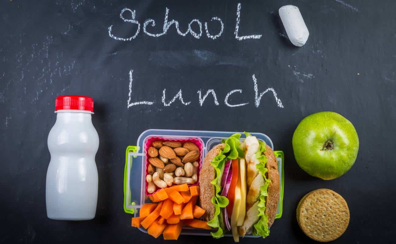 Snack box with vegetables, nuts, apple, and sandwich on blackboard background for healthy school lunch ideas.