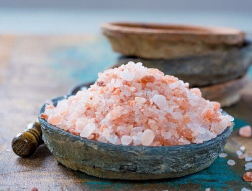 Himalayan pink salt in a rustic bowl with a wooden spoon, emphasizing natural health and wellness ingredients.
