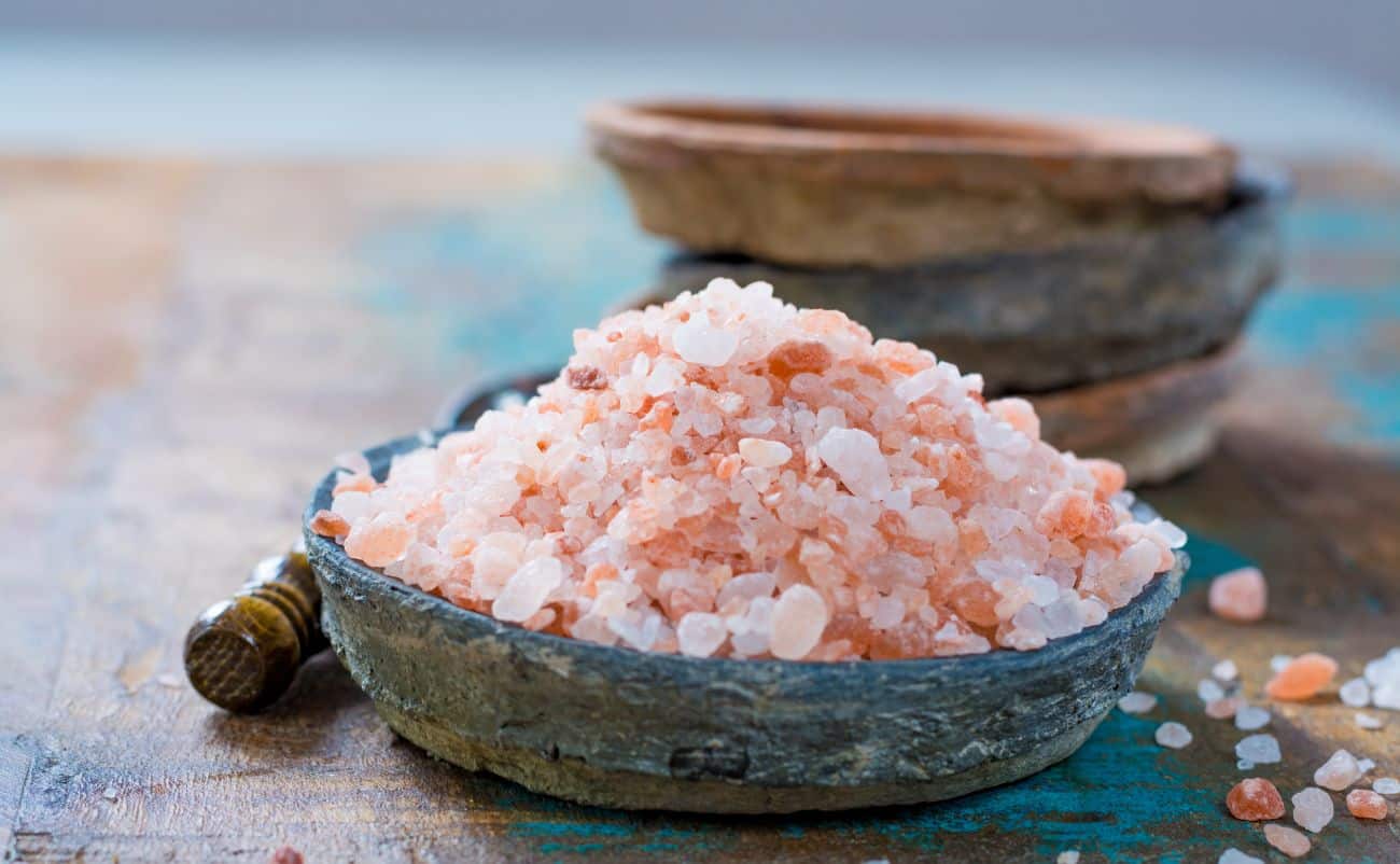 Himalayan pink salt in a rustic bowl with a wooden spoon, emphasizing natural health and wellness ingredients.