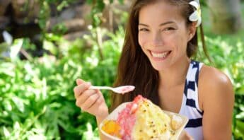 Vibrant woman enjoying a colorful ice cream outdoors in a lush garden setting, embodying healthy fun and leisure.