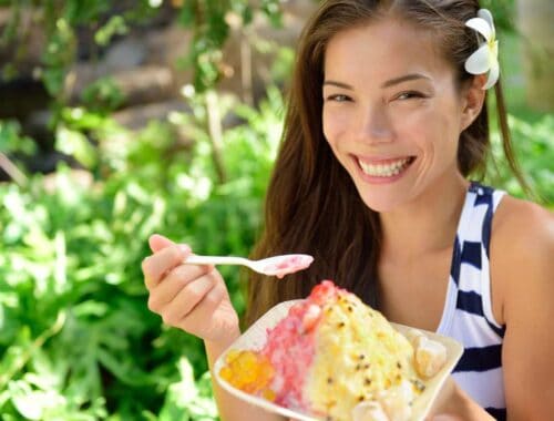 Vibrant woman enjoying a colorful ice cream outdoors in a lush garden setting, embodying healthy fun and leisure.
