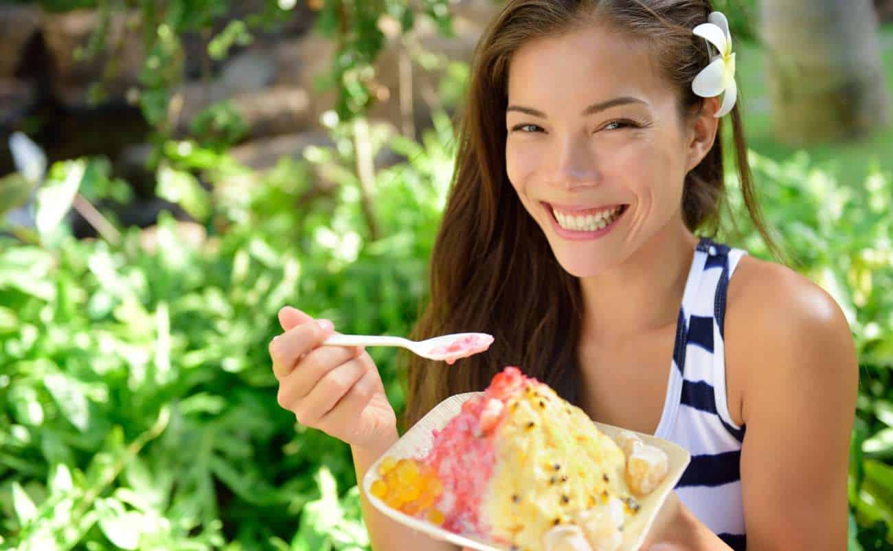 Vibrant woman enjoying a colorful ice cream outdoors in a lush garden setting, embodying healthy fun and leisure.