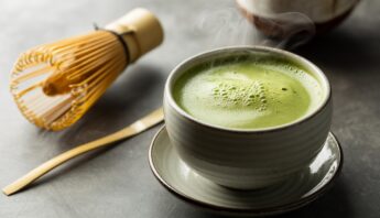 Matcha green tea in a ceramic cup with a bamboo whisk and spoon, highlighting a healthy, antioxidant-rich beverage.
