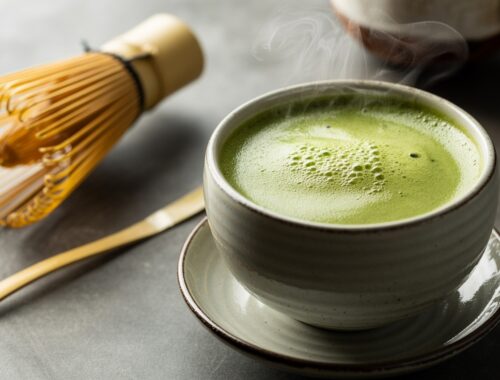 Matcha green tea in a ceramic cup with a bamboo whisk and spoon, highlighting a healthy, antioxidant-rich beverage.