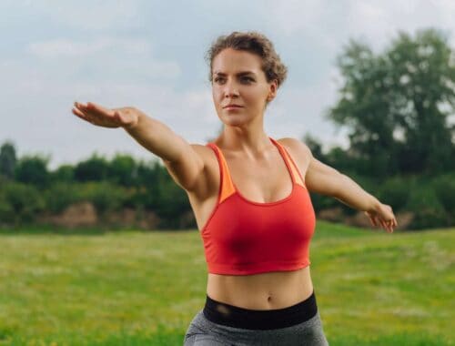Stretching outdoors woman in athletic wear doing arm stretch on green field.