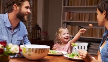 Healthy family meal with smiling parents and child enjoying food together at the dinner table.