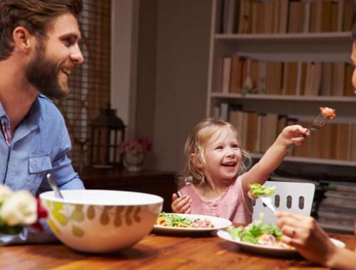 Healthy family meal with smiling parents and child enjoying food together at the dinner table.