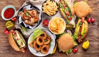 Rich, flavorful fast food meal with burgers, fries, fried onions, and chicken wings on a rustic wooden table with vegetables and dipping sauces.