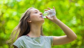 Hydrated young woman drinking water outdoors in a lush green forest for health and fitness.