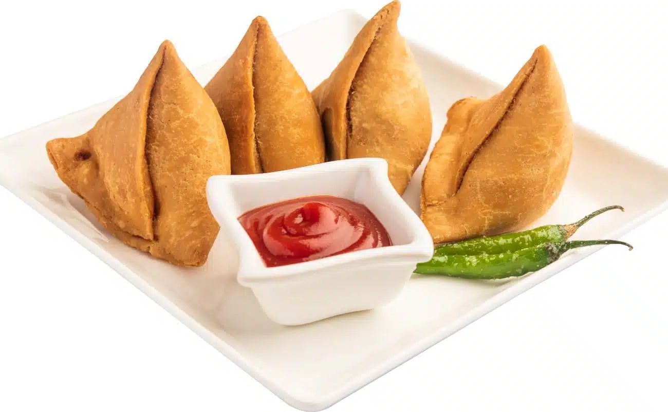 10 Refreshing Summer Veg Side Dishes That Will Elevate Your BBQ Game! 1 Crispy samosas served with ketchup and fresh green chilies on a white plate, an Indian appetizer or snack option.