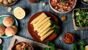 Fresh baby corn on a ceramic plate with herbs, surrounded by salsa, bread rolls, and salad bowls, on a rustic wooden table, highlighting healthy eating and nutritious food options.
