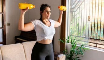 Lifting dumbbells at home for fitness and strength training, woman exercising indoors with natural sunlight, healthy lifestyle, female workout, indoor fitness routine, wellness, and physical activity.