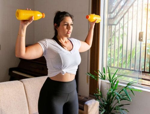 Lifting dumbbells at home for fitness and strength training, woman exercising indoors with natural sunlight, healthy lifestyle, female workout, indoor fitness routine, wellness, and physical activity.