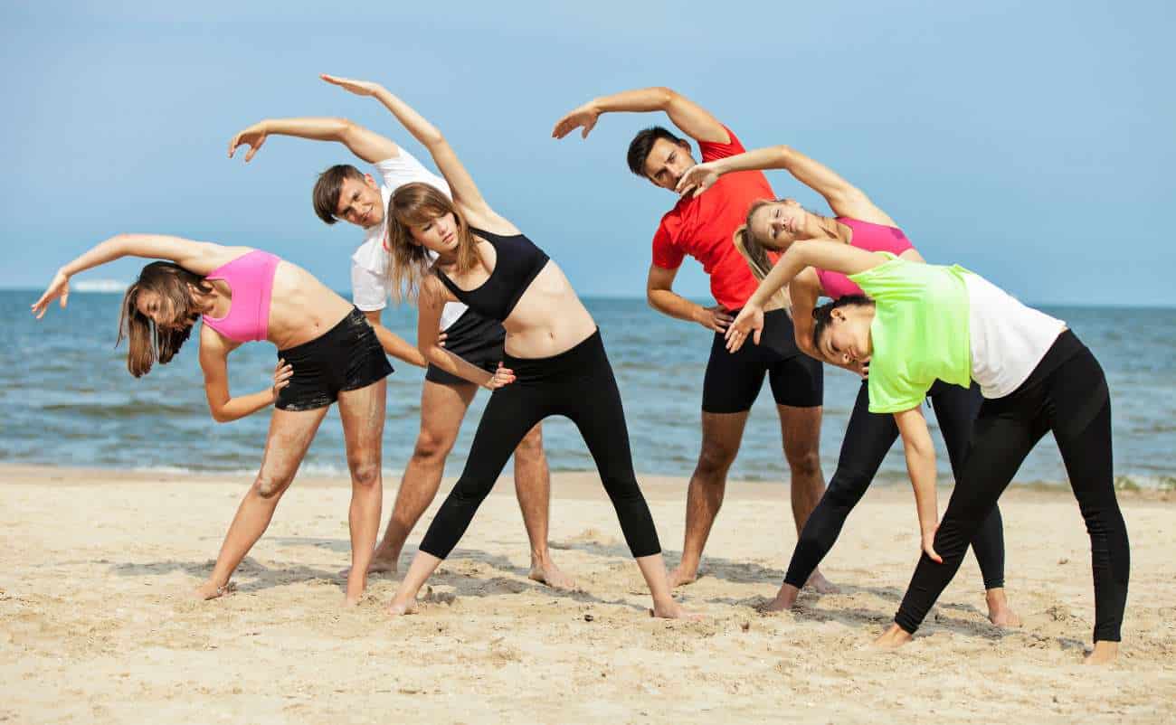 Stretching yoga group on the beach for flexibility and fitness.