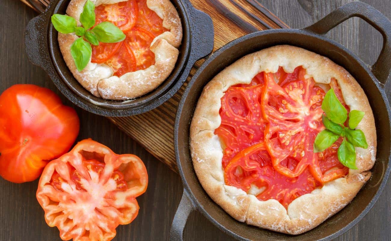Fresh homemade tomato pizza with basil, served in cast iron skillets on a wooden surface, emphasizing healthy and delicious meal options.