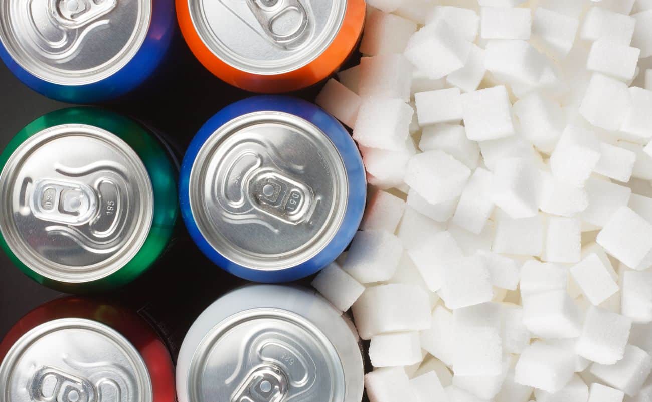 Canned soda cans next to sugar cubes on a black surface, representing unhealthy beverage choices and excess sugar intake.