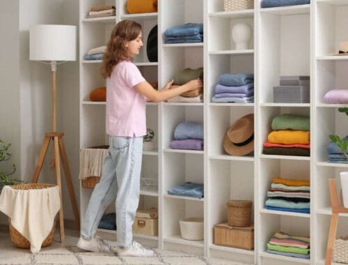 Clothing organization closet, neatly folded towels and clothes on white shelves, woman arranging laundry, home decluttering, interior design for tidy living spaces.
