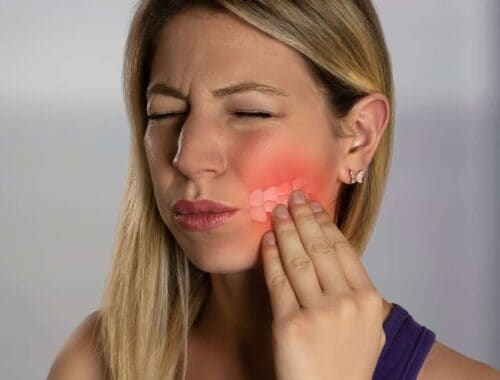 Blonde woman experiencing tooth pain, touching her cheek with a pained expression, highlighting dental discomfort and oral health issues.