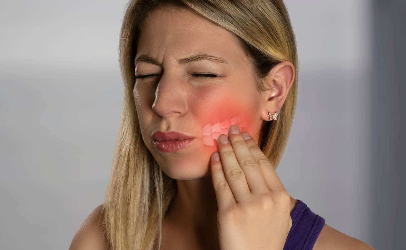 Blonde woman experiencing tooth pain, touching her cheek with a pained expression, highlighting dental discomfort and oral health issues.